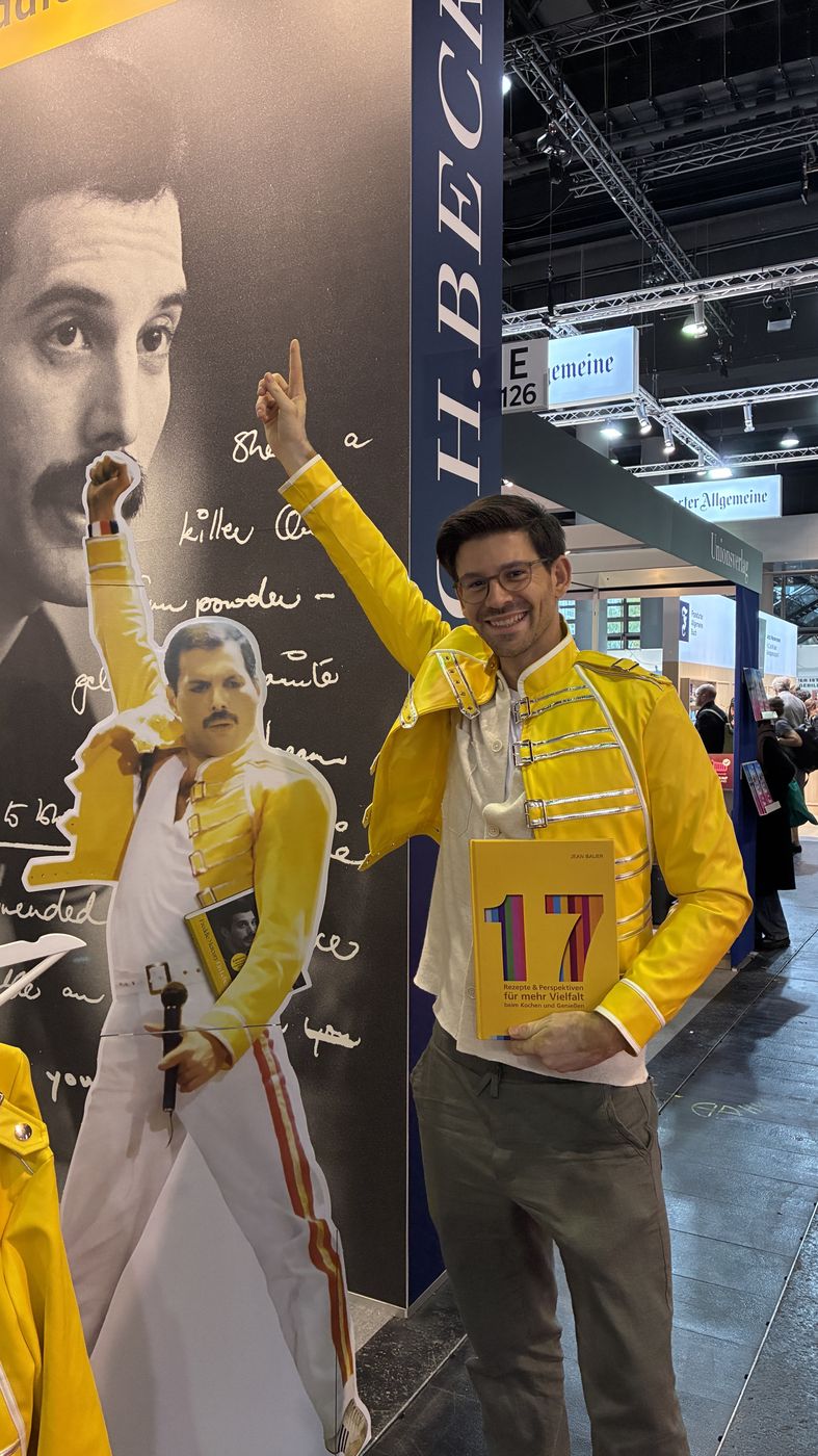 Jean Bauer in gelber Jacke mit dem Buch auf der Messe