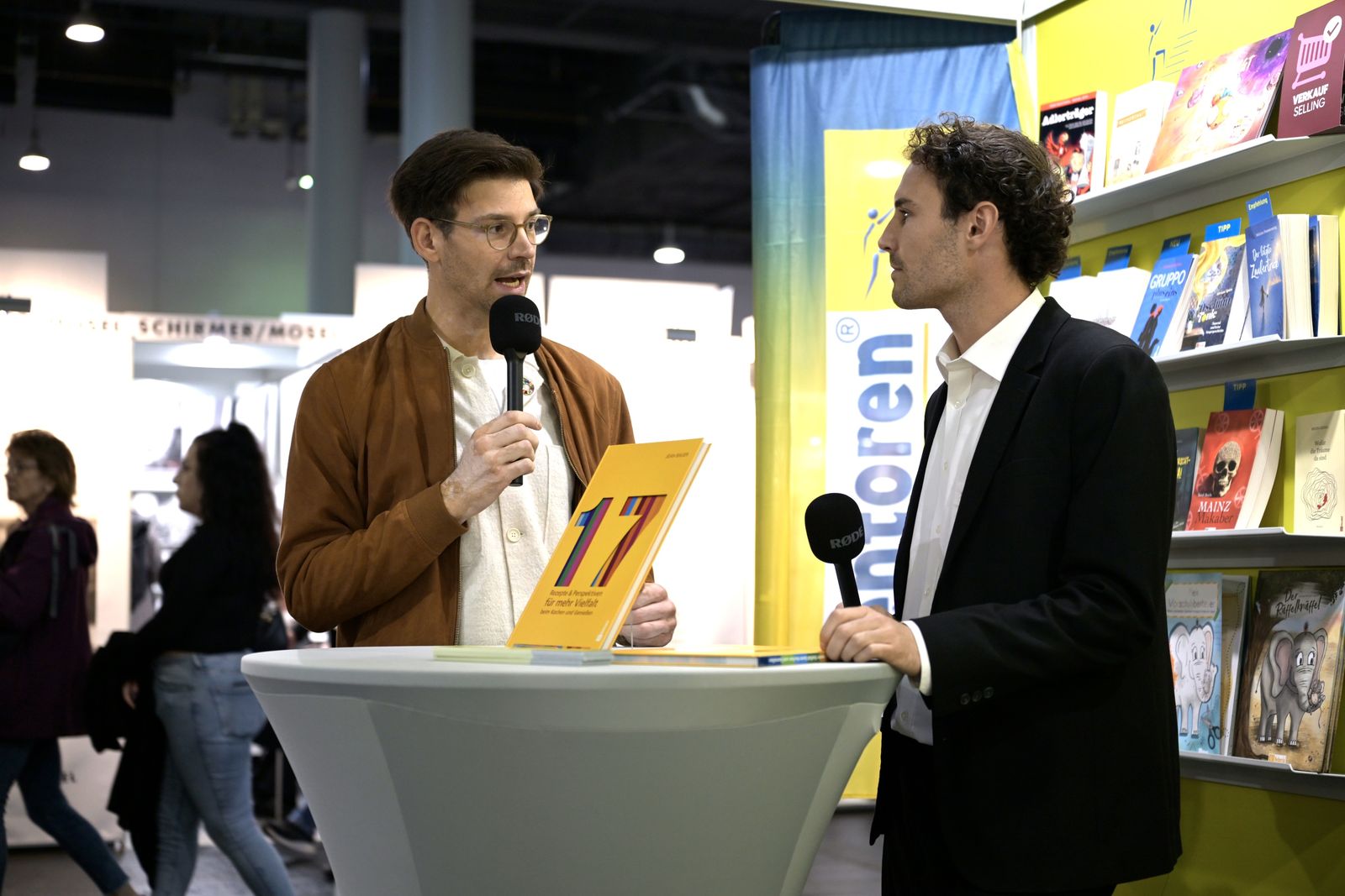 Bühnengespräch am Messestand: Jean Bauer mit Mikrofon und dem Buch „17“
